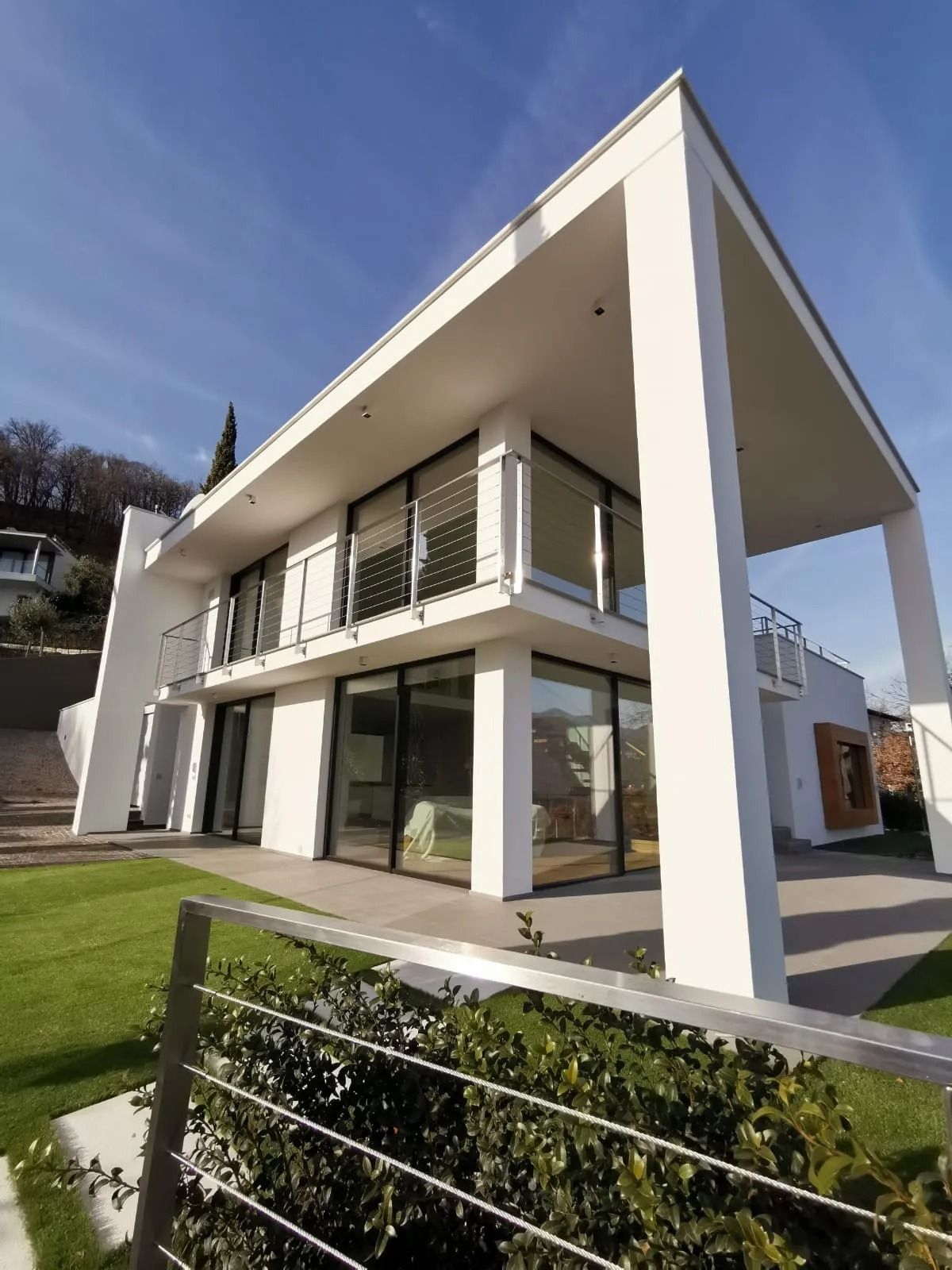 Casa moderna a due piani di colore bianco, con ampie finestre e tetto spiovente, vista dal prato antistante.