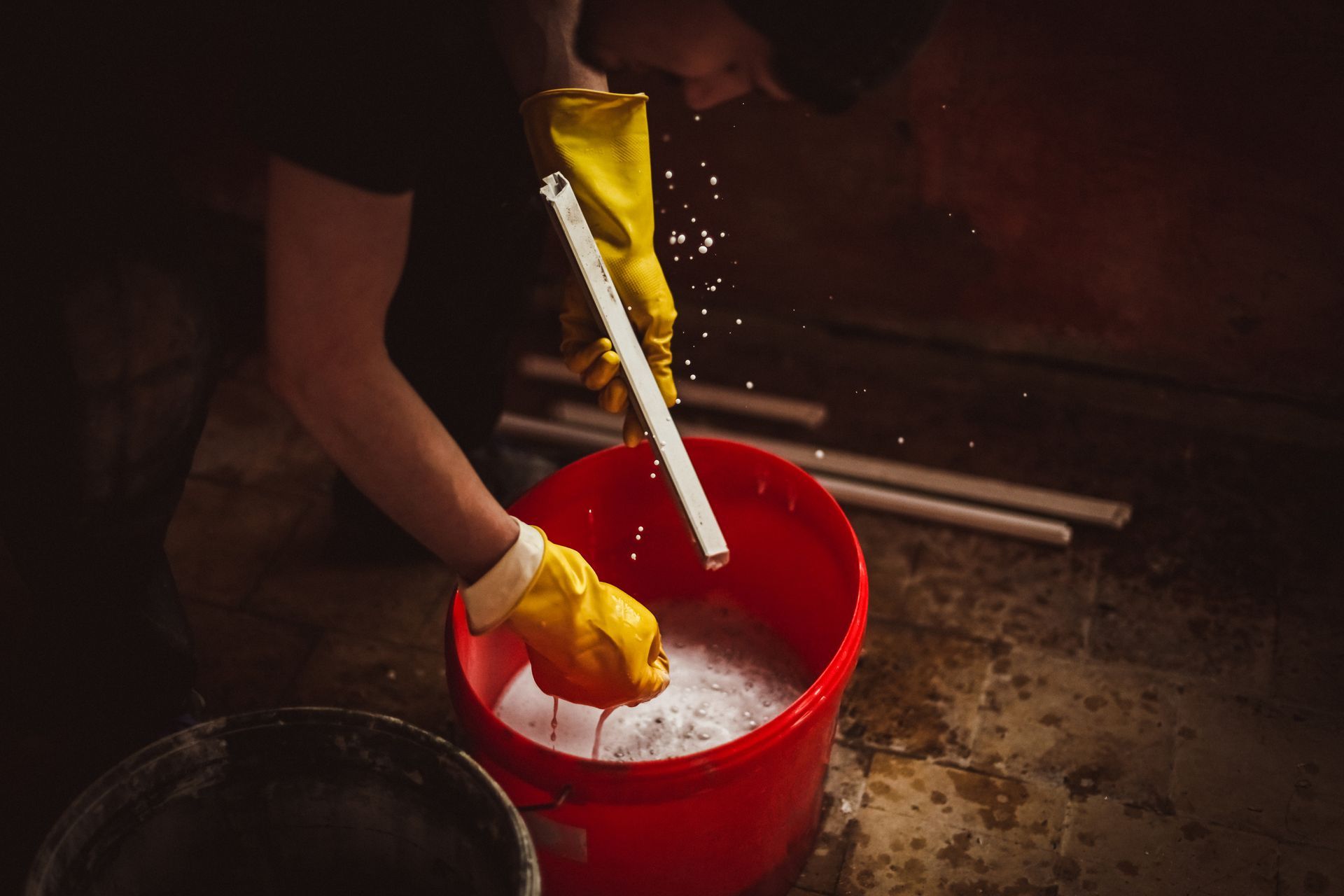Person wearing yellow gloves mixing white powder in a red bucket outdoors at night