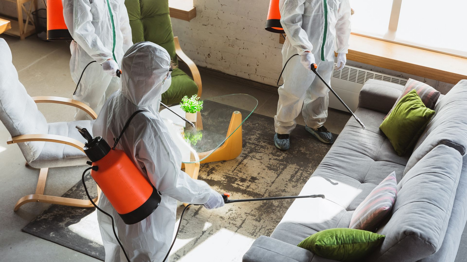 People in protective suits spraying disinfectant in a living room.