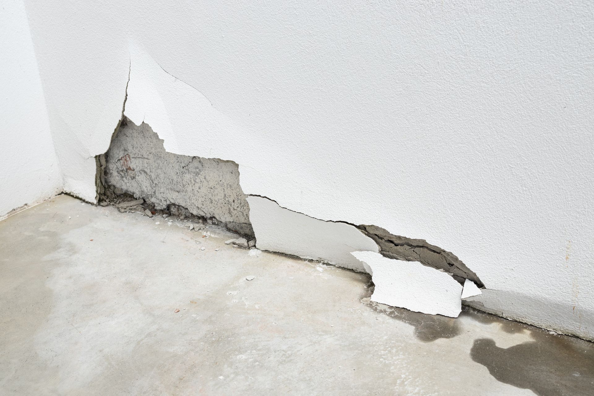 Peeling white wall with cracked plaster and water damage along the floor