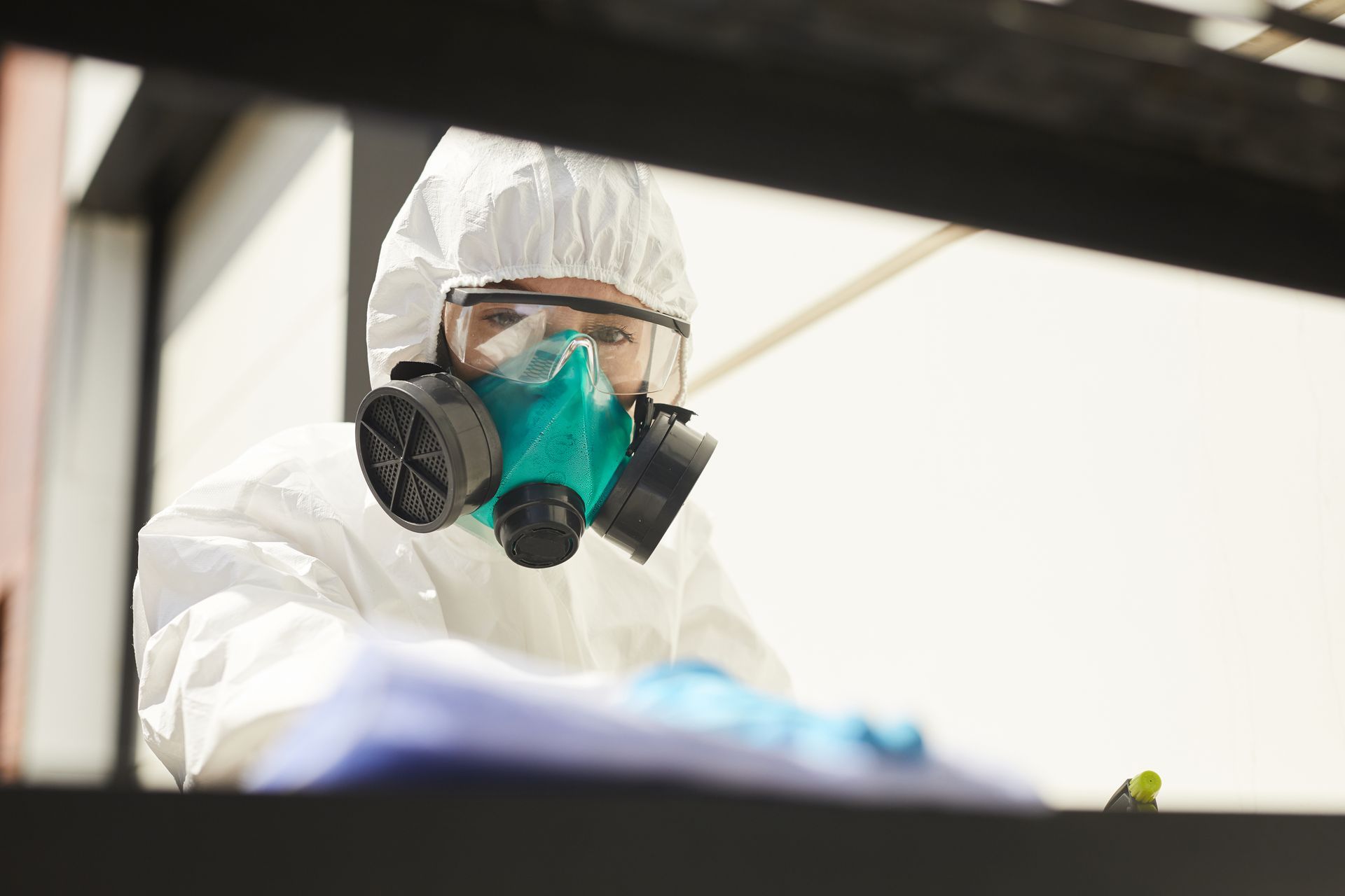 A person in a white hazmat suit and a teal respirator mask with goggles works indoors.