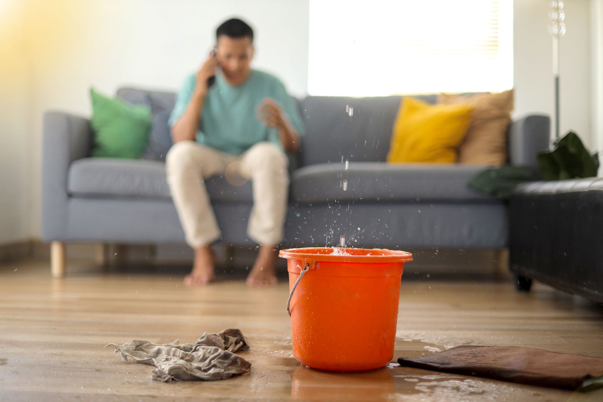 Spilled orange paint bucket on a wooden floor, with a blurred person sitting on a couch in the background
