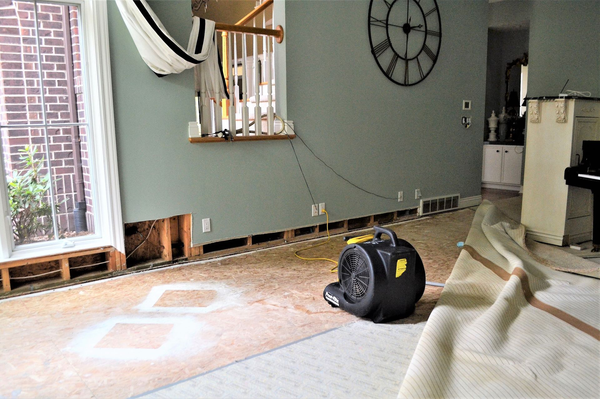 Damaged living room floor with exposed subfloor, a box fan, and dust from repairs