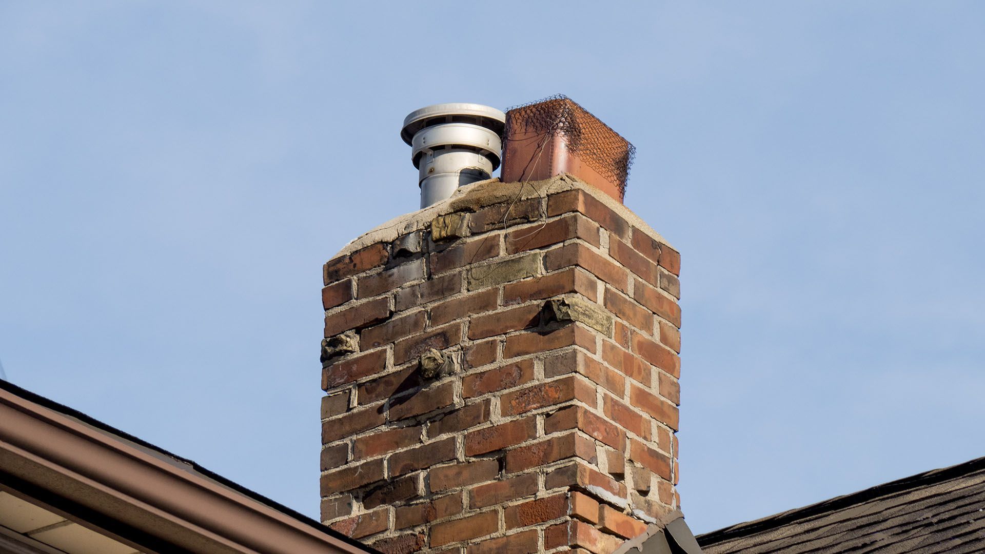 Brick chimney with a metal cap against a blue sky.