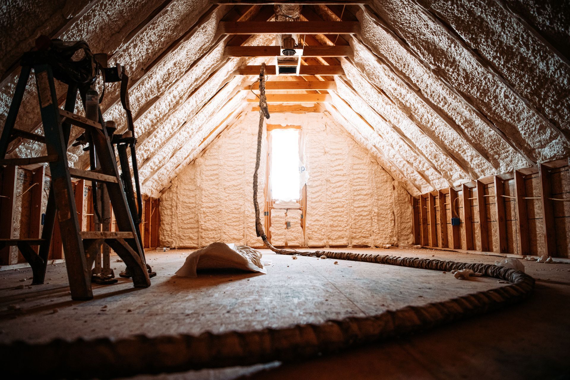 Attic under construction with exposed rafters, brick walls, wooden ladder, and insulation on the floor