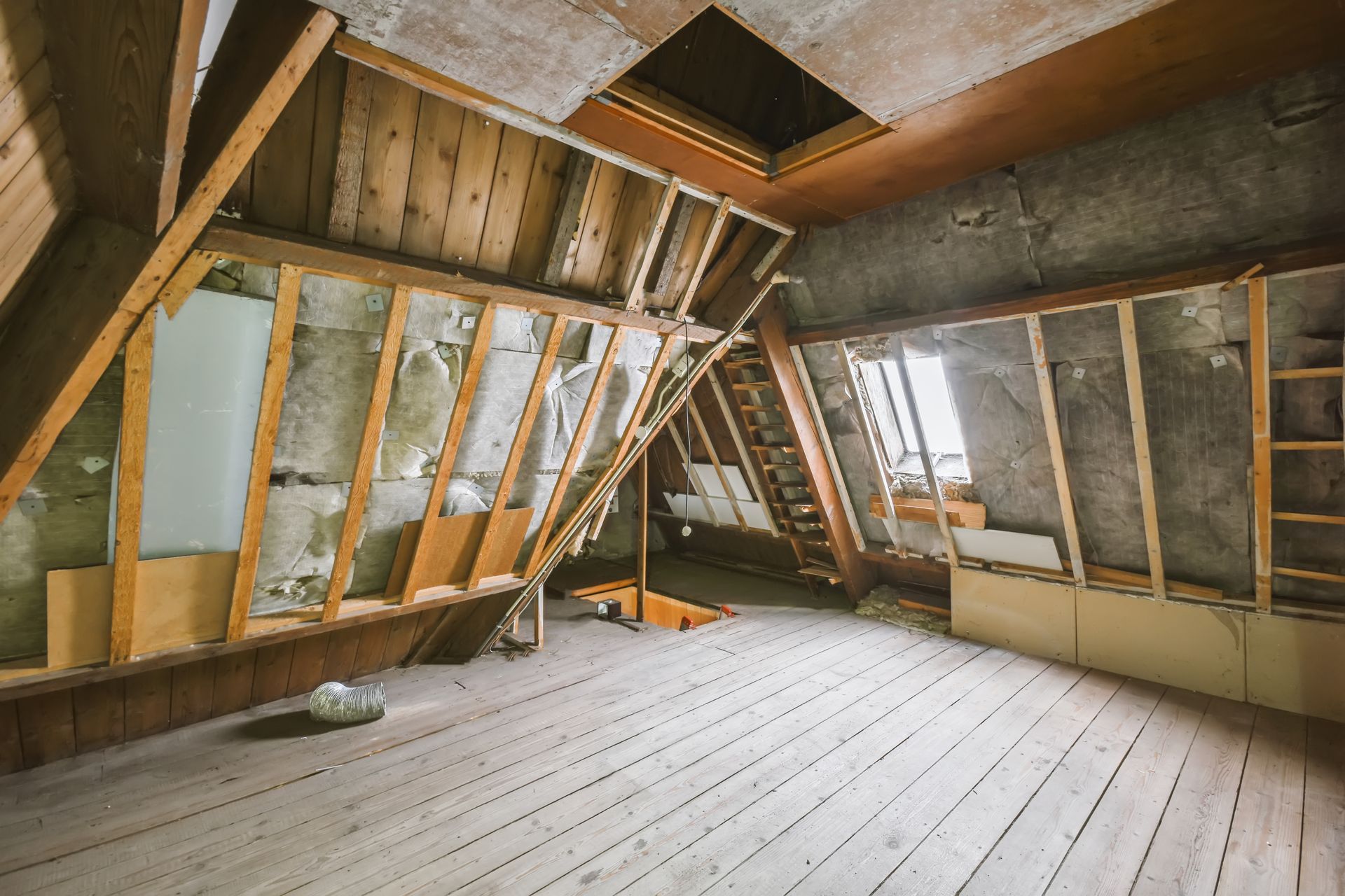 Damaged attic interior with exposed wooden framing, slanted walls, and unfinished floorboards