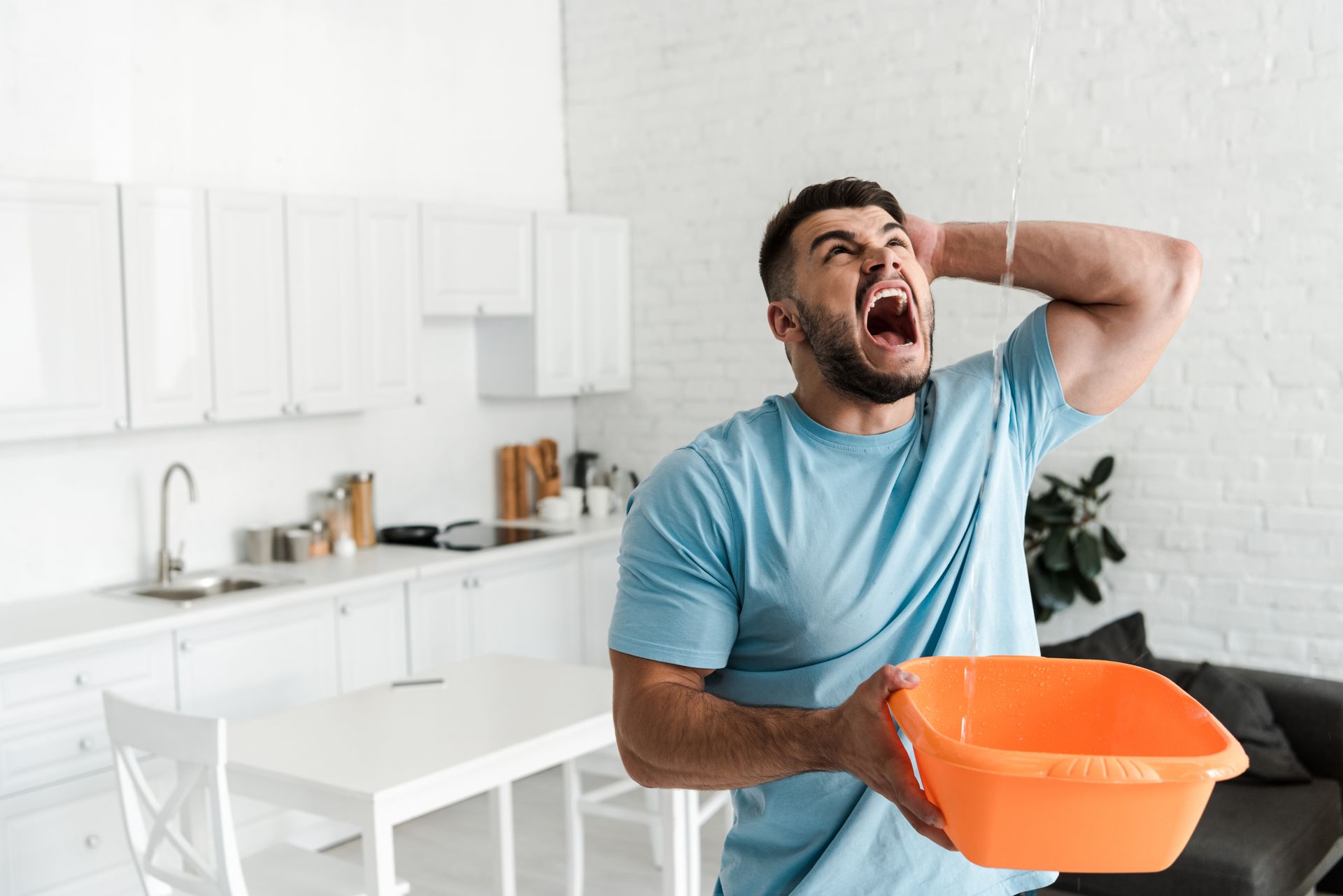 Man in a bright kitchen, holding an orange bucket and yawning with a hand over his face