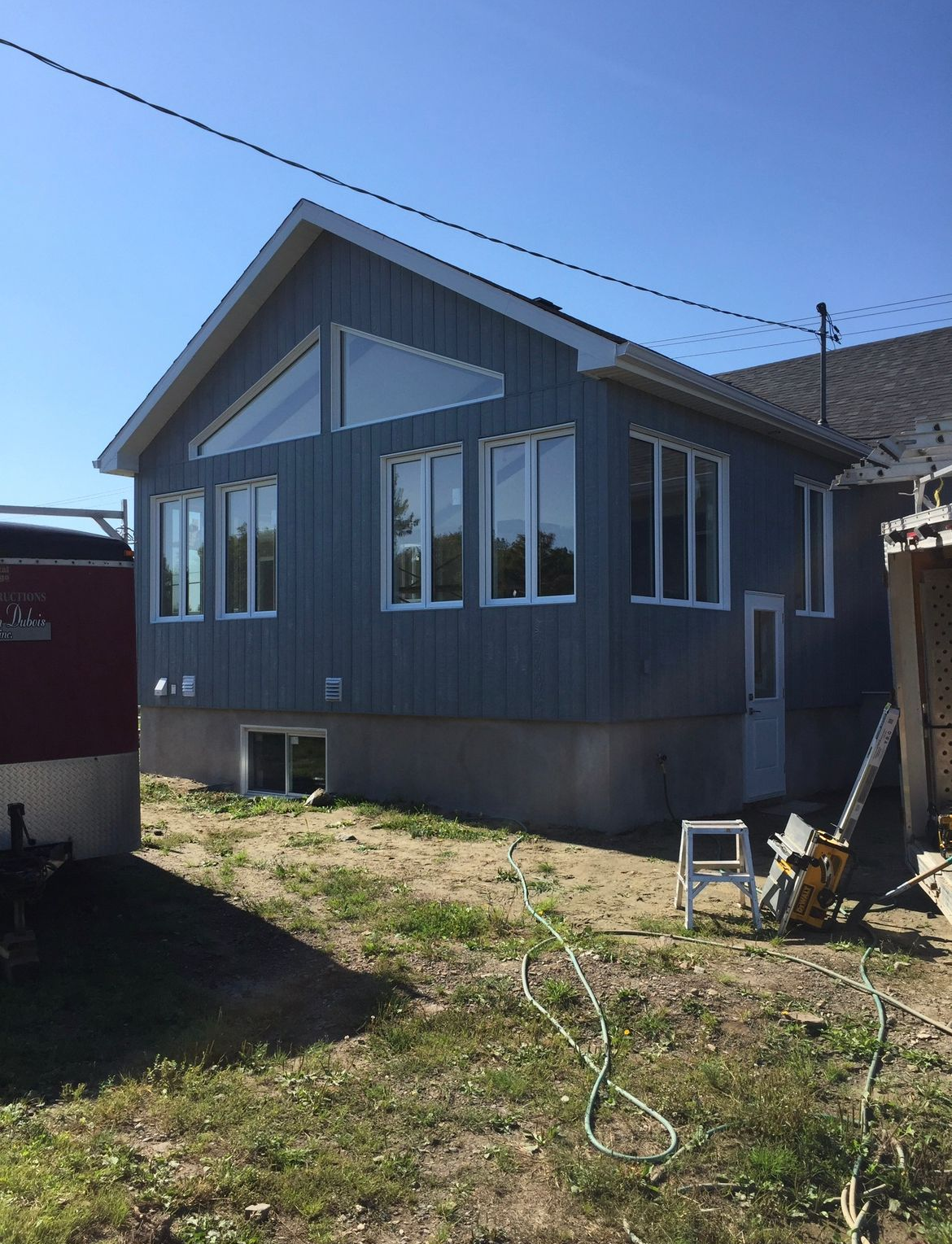 Extension de maison aux murs bleus, avec de grandes fenêtres, des boiseries blanches et une petite porte. Cadre extérieur ensoleillé.