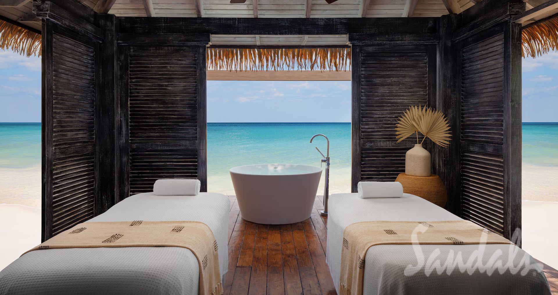 Spa treatment room overlooking the ocean, with massage tables and a bathtub.