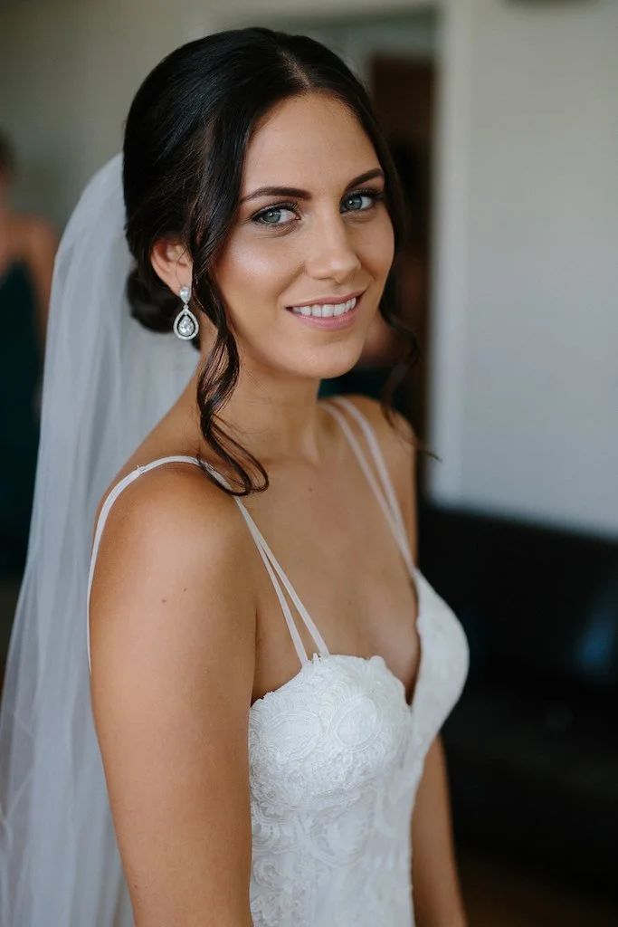 A woman in a wedding dress and veil is smiling for the camera.