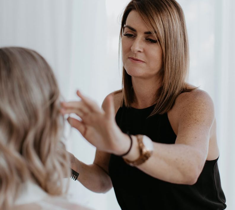 A woman in a black top is looking at her hair in a mirror.