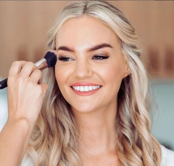 A woman is smiling while applying makeup to her face
