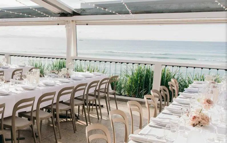 A long table and chairs set up for a wedding reception with a view of the ocean.