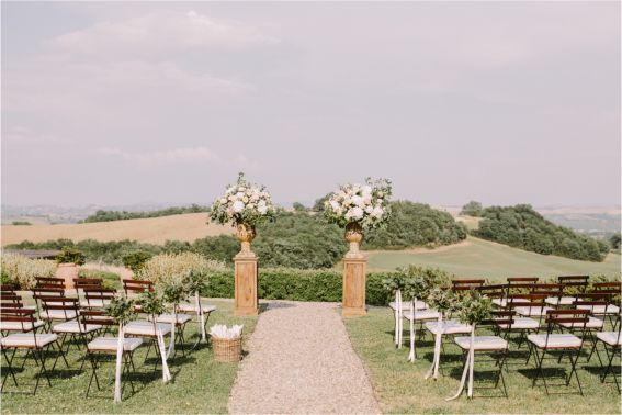 A wedding ceremony is taking place in a field with flowers in vases.