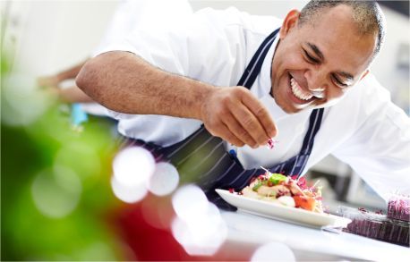 A chef is smiling while decorating a plate of food.
