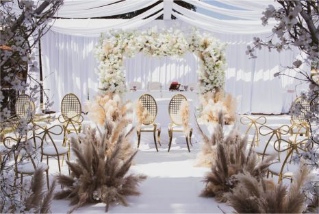 A wedding ceremony is being held under a canopy with flowers and chairs.