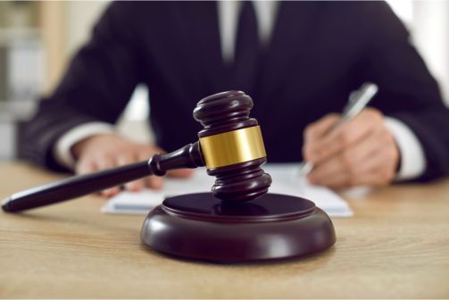 A judge is writing on a piece of paper next to a wooden gavel.