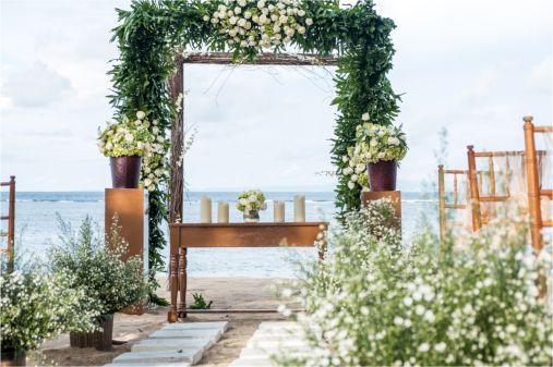 A wedding arch decorated with flowers and candles on the beach.
