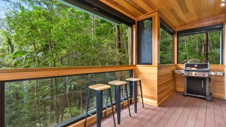 A balcony with a grill and stools and a view of the woods.