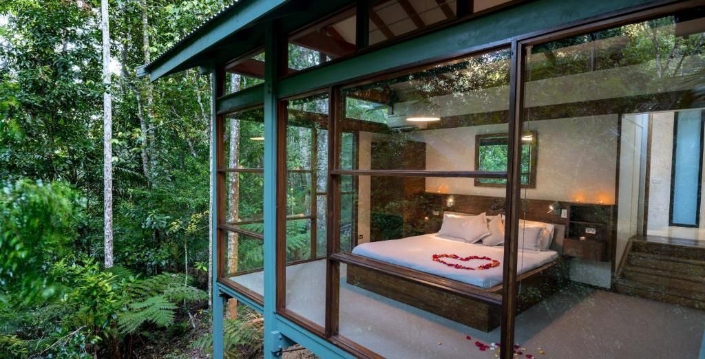 A bedroom with a large bed and a lot of windows surrounded by trees.