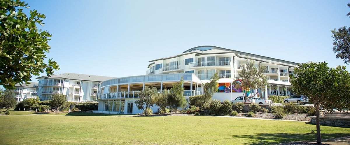 A large white building with a lot of windows is surrounded by trees and grass.