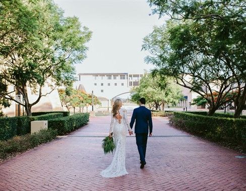 A bride and groom are walking down a brick walkway holding hands.