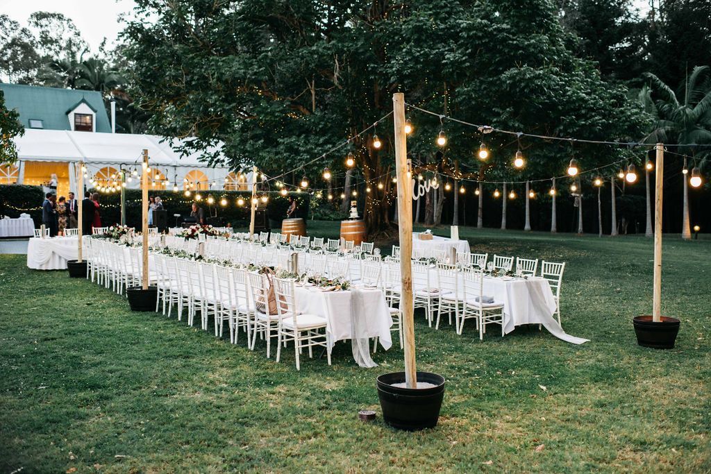 A long row of tables and chairs under a tent in a field.