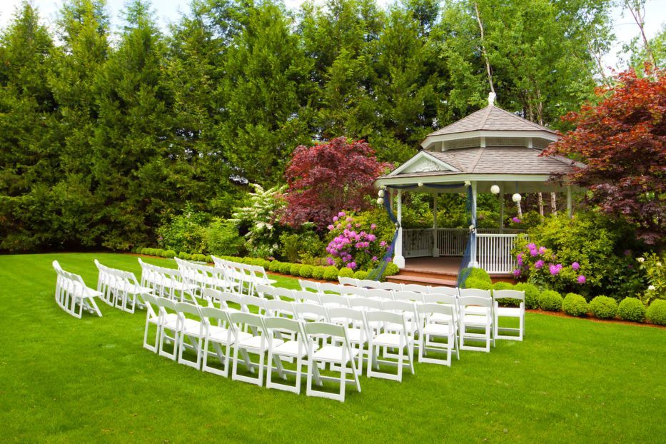A row of white chairs are lined up in front of a gazebo.