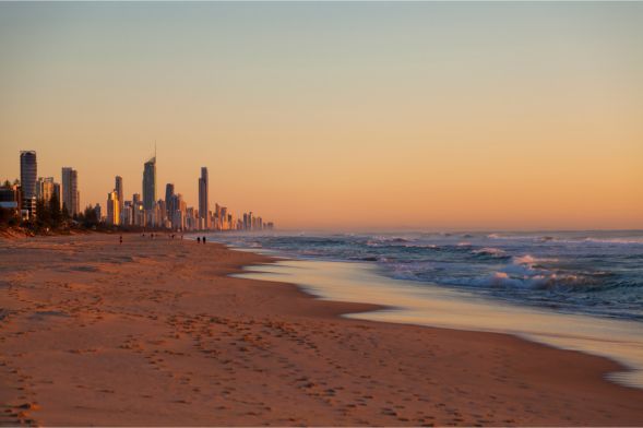 A beach with a city skyline in the background at sunset.