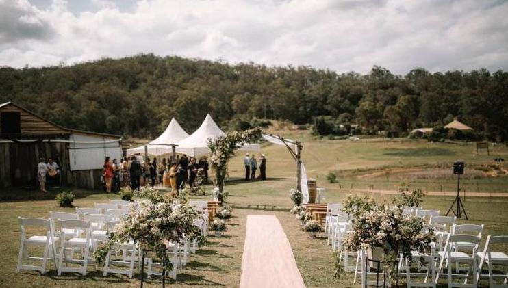 A wedding ceremony is taking place in a field with white chairs and flowers.
