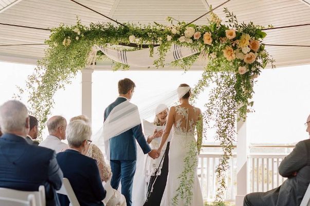 A bride and groom are holding hands during their wedding ceremony under a gazebo.