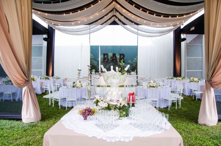 A table with glasses and flowers on it in front of a tent.