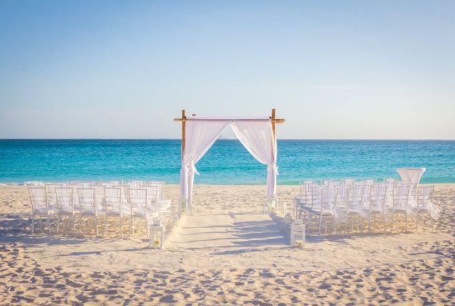 A beach with a canopy and chairs set up for a wedding ceremony.