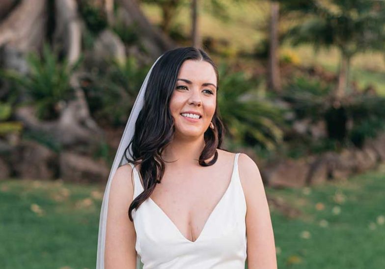A bride in a white dress and veil is smiling for the camera.