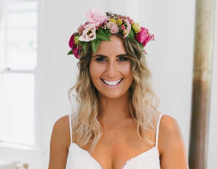 A woman wearing a flower crown and a white dress is smiling.