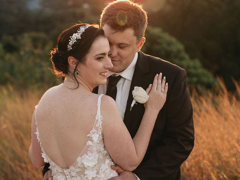 A bride and groom are posing for a picture in a field.