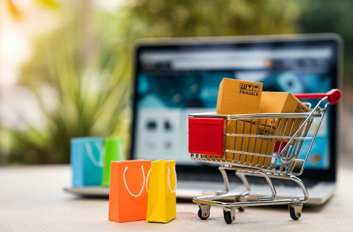 A shopping cart filled with boxes and shopping bags in front of a laptop computer.