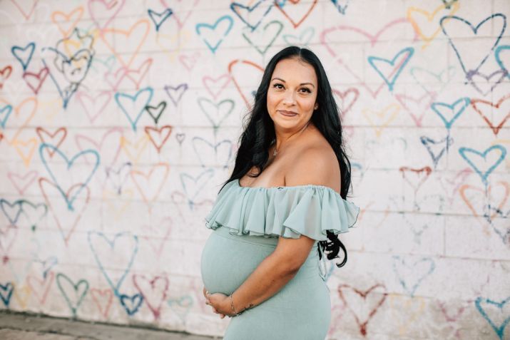 A pregnant woman is standing in front of a wall with hearts painted on it.