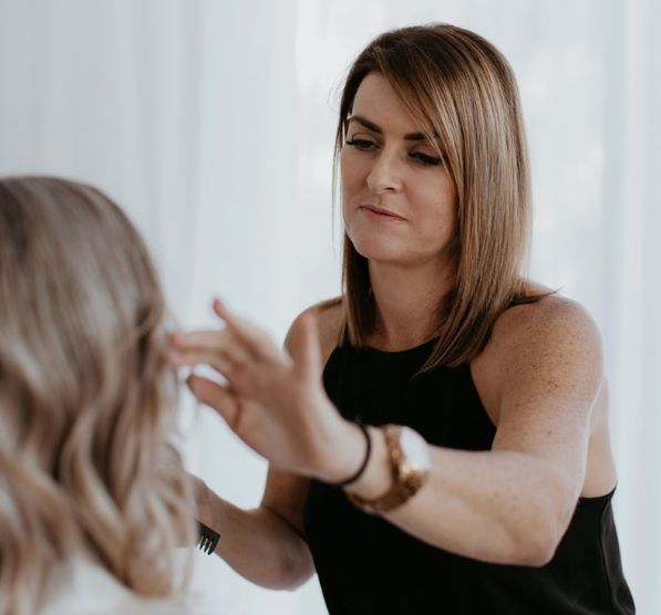A woman in a black tank top is looking at another woman 's hair.