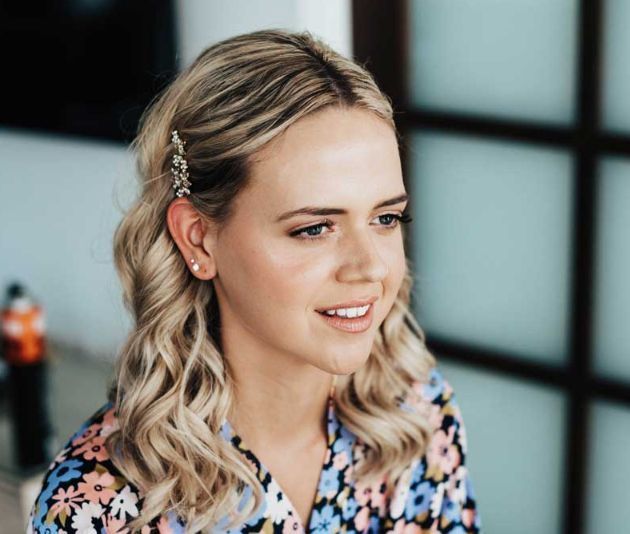 A woman with blonde hair is wearing a floral shirt and earrings.