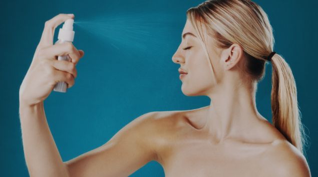 A woman is spraying a spray bottle on her face.