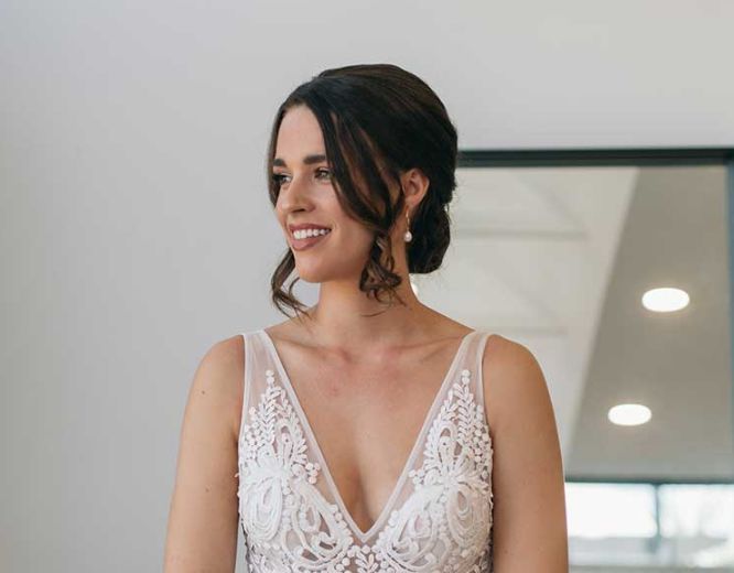 A woman in a wedding dress is smiling in front of a mirror.