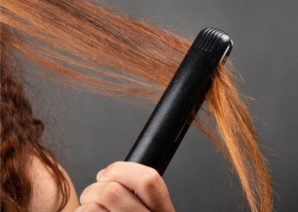 A woman is straightening her hair with a flat iron.