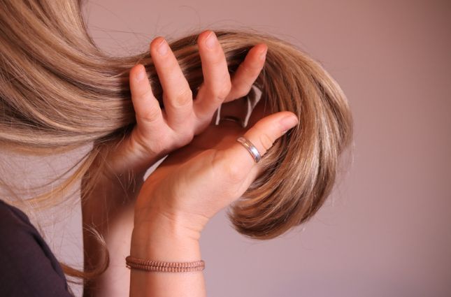 A woman with a ring on her finger is touching her hair.