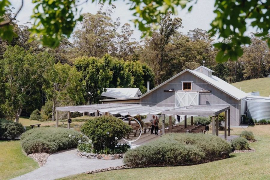 A gray barn with a white door is surrounded by trees