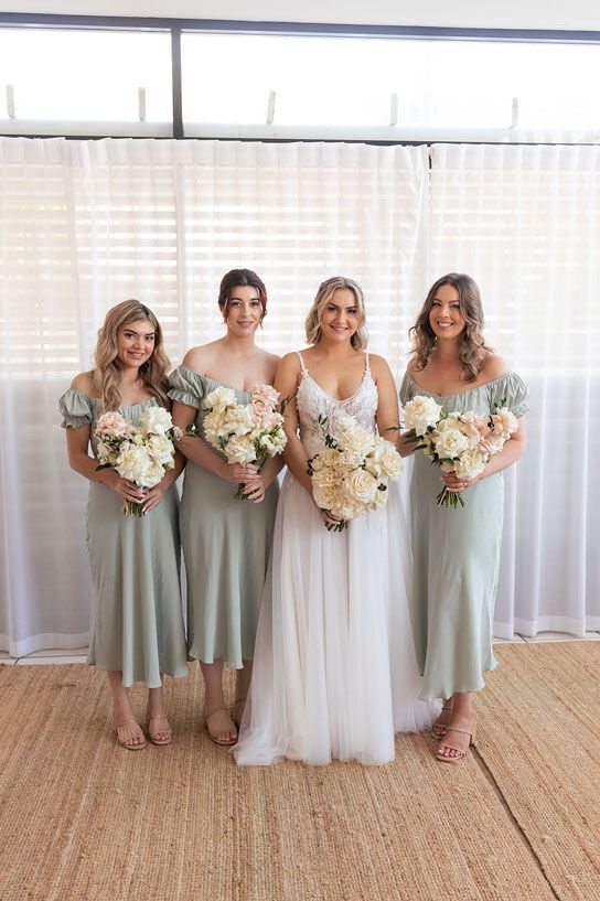 A bride and her bridesmaids are posing for a picture while holding bouquets of flowers.