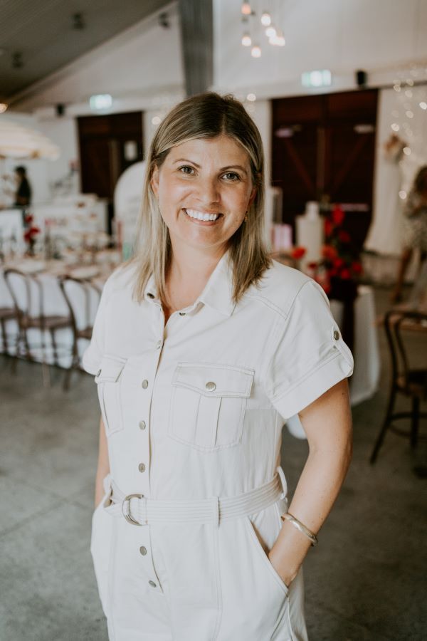 A woman in a white jumpsuit is standing in a room with her hands in her pockets.
