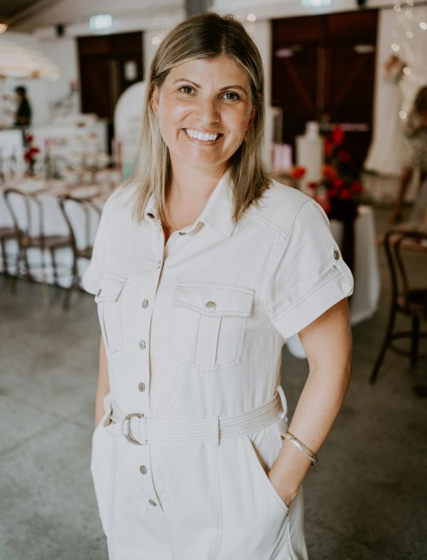 A woman in a white jumpsuit is standing in a room with her hands in her pockets.