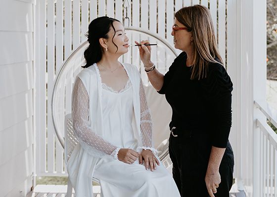A woman is applying makeup to a woman sitting in a chair.