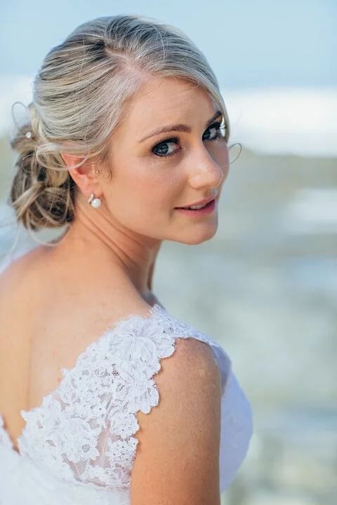 A woman in a wedding dress is standing on the beach looking over her shoulder.